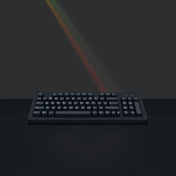 Un clavier de micro-ordinateur rétro noir avec des touches en gomme grises reposant sur une surface sombre polie sous de doux rayons de lumière arc-en-ciel.